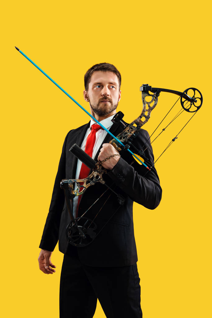 Geschäftsmann zielt mit Pfeil und Bogen auf Zielscheibe, isoliert auf gelbem Hintergrund - Foto, Bild