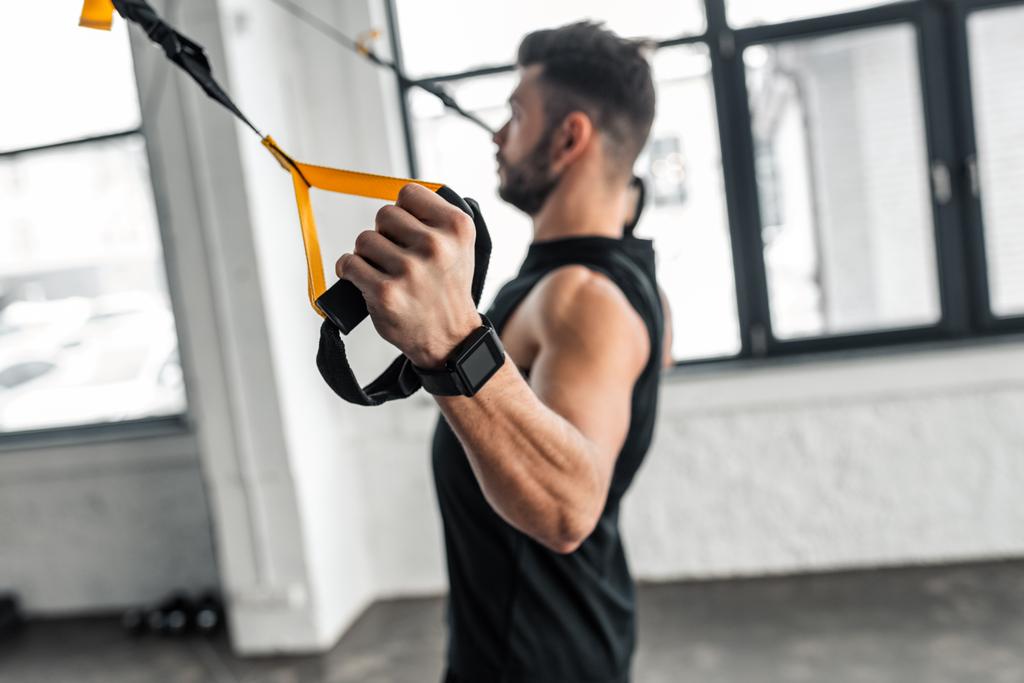 Seitenansicht eines muskulösen jungen Mannes im Sportbekleidungstraining mit Widerstandsbändern im Fitnessstudio - Foto, Bild