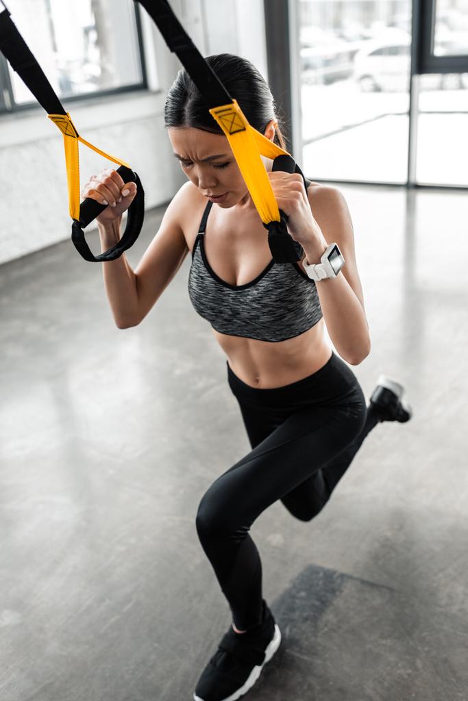 visão de alto ângulo de focado jovem desportista exercitando com tiras de suspensão no ginásio
  - Foto, Imagem