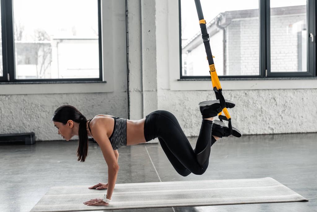 vista lateral de hermosa chica deportiva haciendo ejercicio con bandas de resistencia en la estera de yoga en el gimnasio
  - Foto, imagen