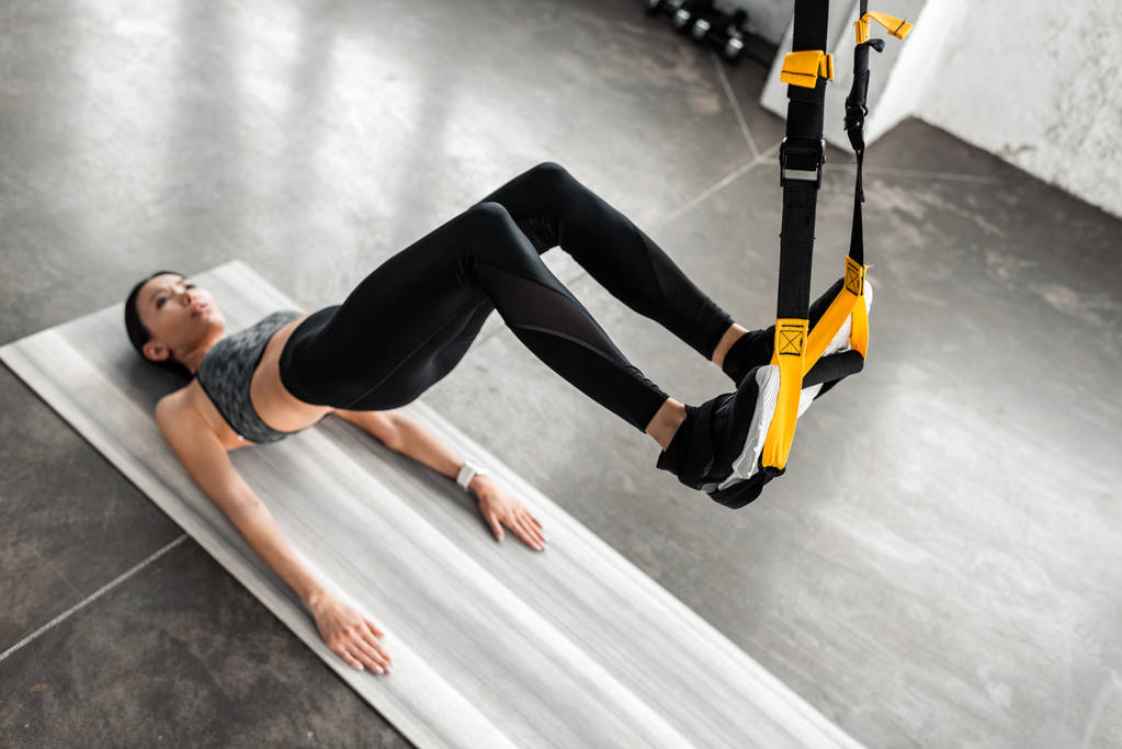 vista ad alto angolo della ragazza sportiva appesa alle cinghie di fitness e allenamento sul tappetino yoga in palestra
 - Foto, immagini