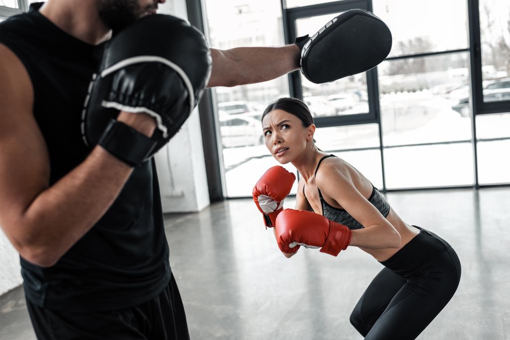 tiro recortado de entrenador masculino haciendo ejercicio con chica deportiva en guantes de boxeo en el gimnasio
  - Foto, Imagen