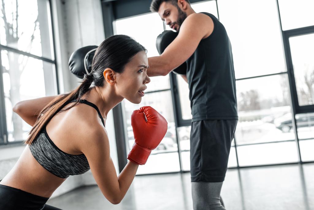 jovem esportista concentrado em luvas de boxe exercitando-se com treinador no ginásio
 - Foto, Imagem
