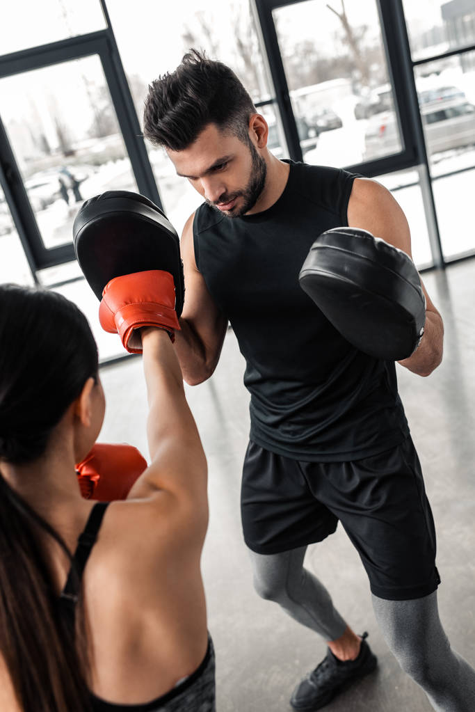 Oříznout záběr sportovkyně v Boxerské rukavice cvičení s trenérem v posilovně - Fotografie, Obrázek