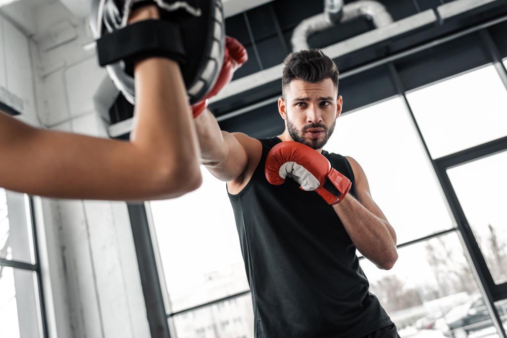 частковий вигляд тренера і чоловіка-боксера в тренуванні боксерських рукавичок разом у спортзалі
   - Фото, зображення