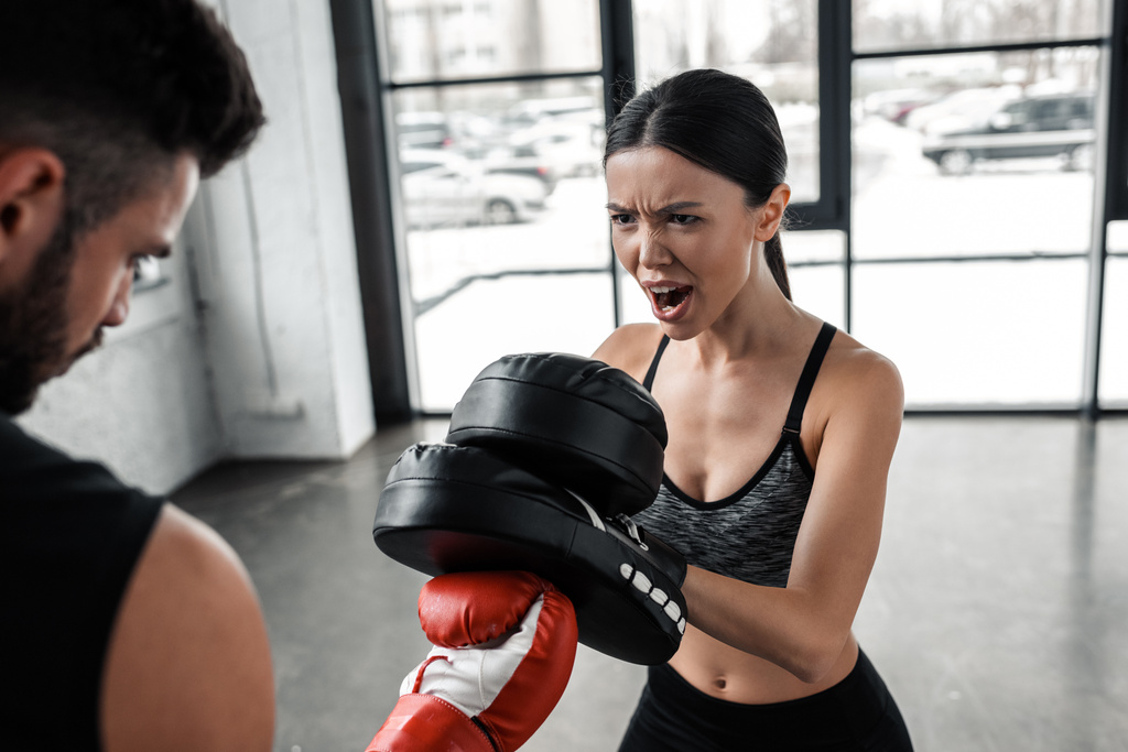 Schnappschuss von emotionaler Sportlerin, die jungen Boxer beim Training im Fitnessstudio anbrüllt - Foto, Bild