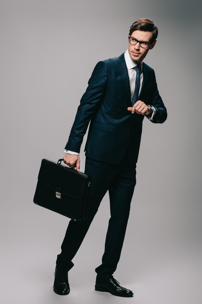 серйозний бізнесмен, що стоїть у костюмі з портфелем на сірому фоні
  - Фото, зображення