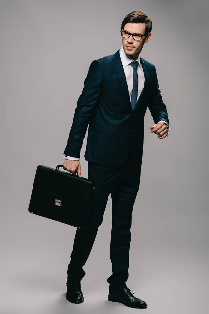 vážný podnikatel v obleku drží aktovku na šedém pozadí  - Fotografie, Obrázek