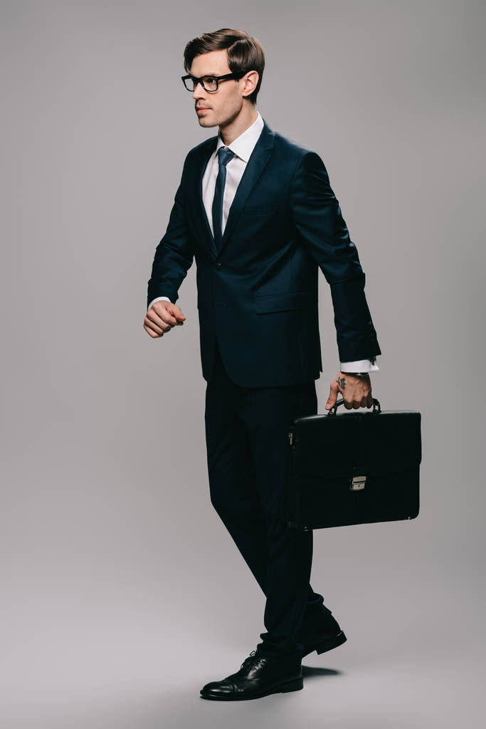 Jistý podnikatel v obleku chůzi s Aktovkou na šedém pozadí  - Fotografie, Obrázek