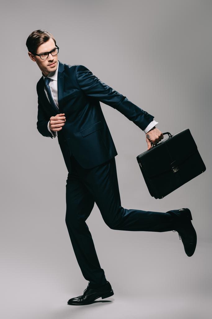 hombre de negocios confiado en traje corriendo con maletín sobre fondo gris
  - Foto, imagen