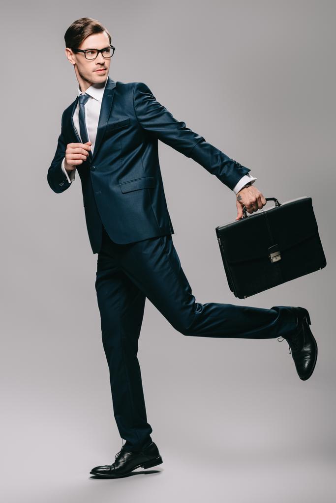 handsome businessman in suit running with briefcase on grey background  - Photo, Image
