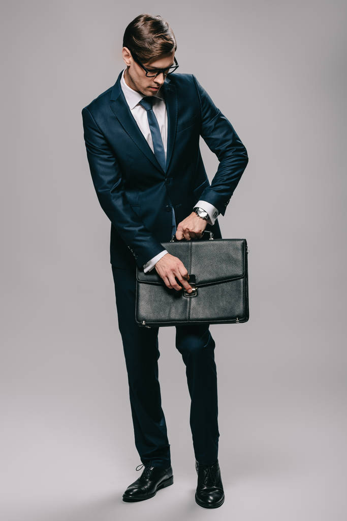 красивый бизнесмен в очках открывает портфель на сером фоне
  - Фото, изображение