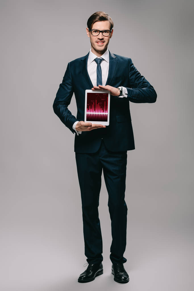 guapo hombre de negocios sosteniendo tableta digital con gráficos en pantalla sobre fondo gris
  - Foto, Imagen