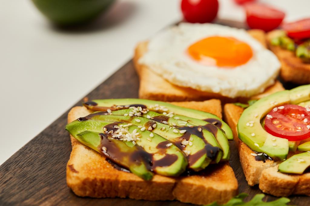 kesme tahtası tost, çırpılmış yumurta, domates ve beyaz arka plan üzerinde avokado ile seçici odak - Fotoğraf, Görsel