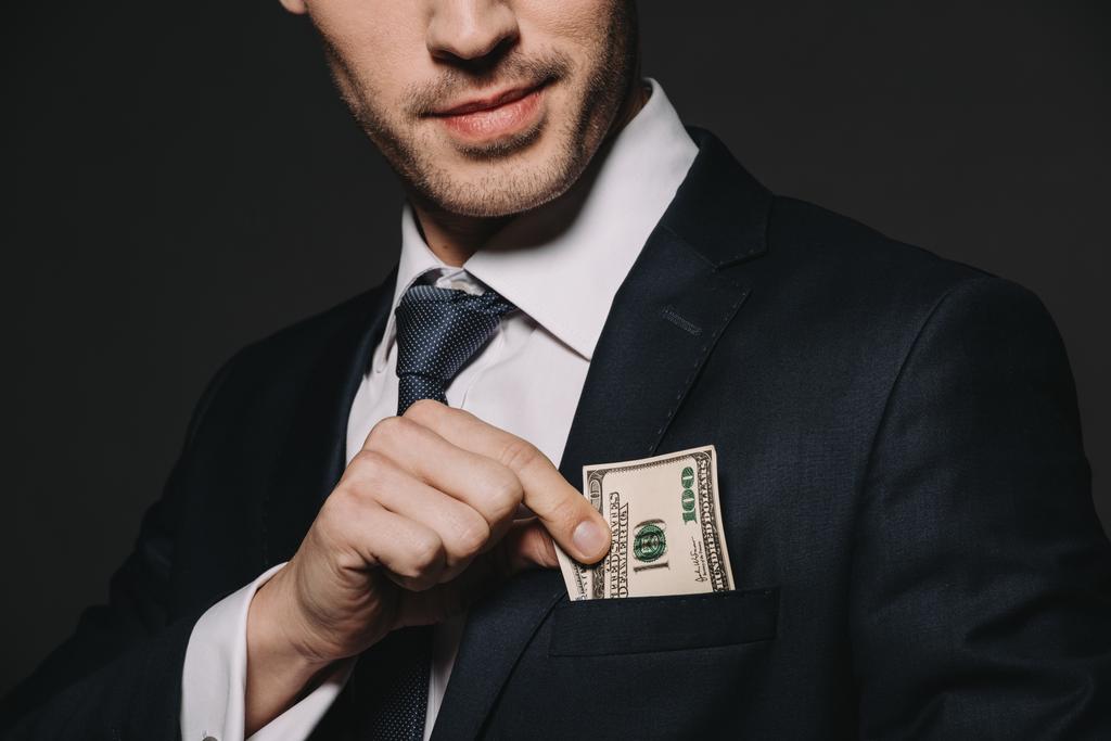bijgesneden weergave van zakenman dollar bankbiljet aanbrengend zak geïsoleerd op zwart - Foto, afbeelding