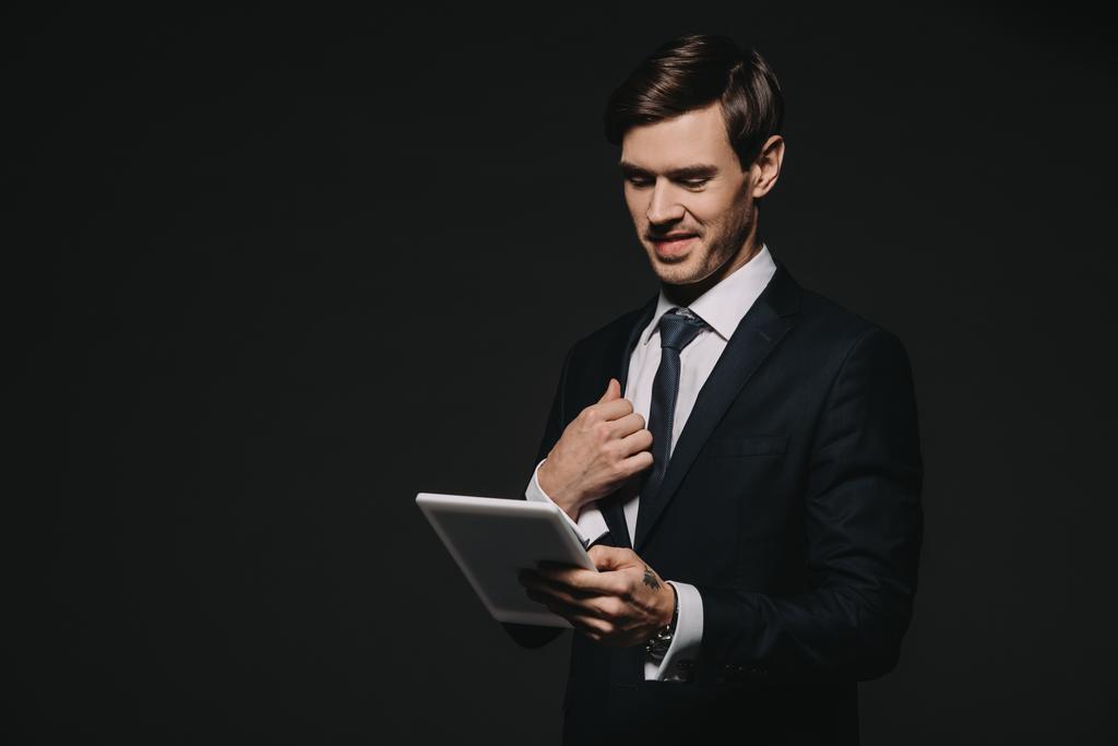 улыбающийся бизнесмен, держащий в руках цифровой планшет, изолированный на черном
 - Фото, изображение