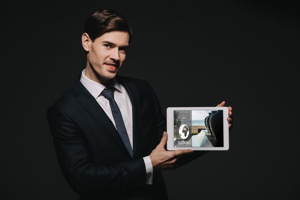homme d'affaires joyeux tenant tablette numérique avec application de réservation à l'écran isolé sur noir
 - Photo, image