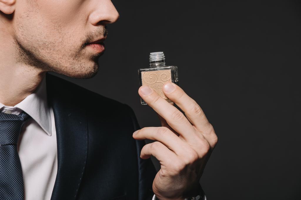 vista recortada del hombre en traje oliendo perfume aislado en negro
 - Foto, imagen