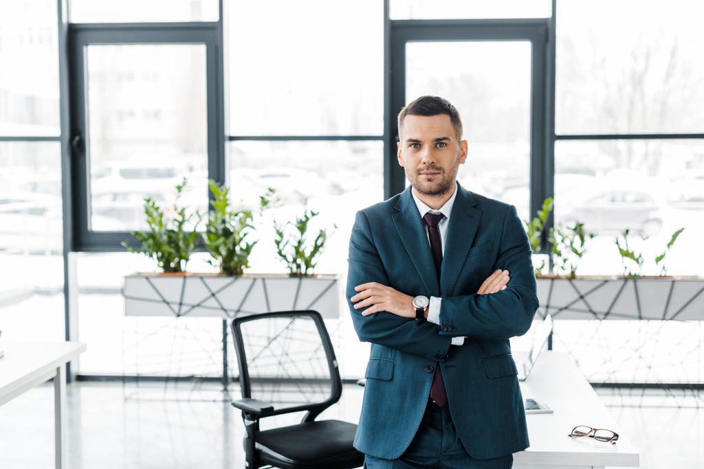 komea liikemies seisoo ristissä kädet modernissa toimistossa
  - Valokuva, kuva