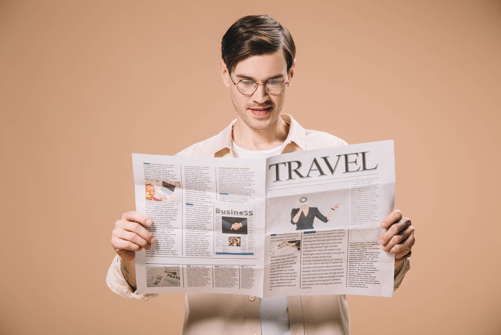 όμορφος άνδρας στο γυαλιά ανάγνωσης ταξίδια εφημερίδα απομονώνονται σε μπεζ  - Φωτογραφία, εικόνα