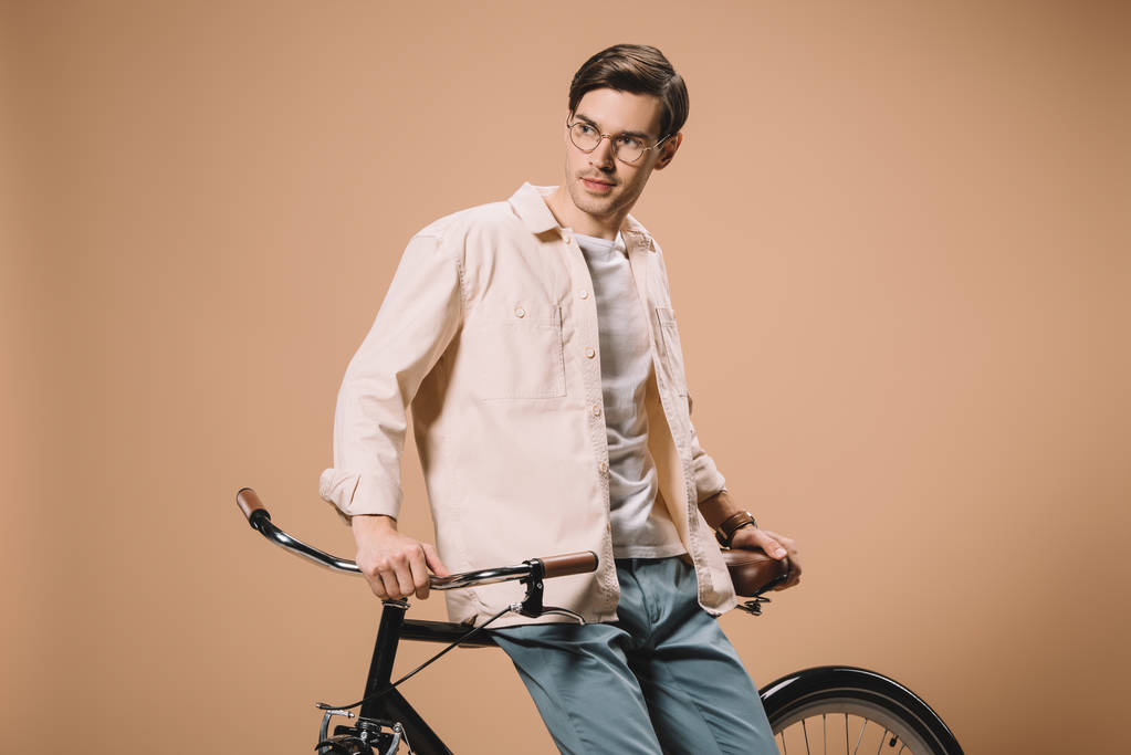 красивий чоловік стоїть біля велосипеда ізольовано на бежевому
  - Фото, зображення