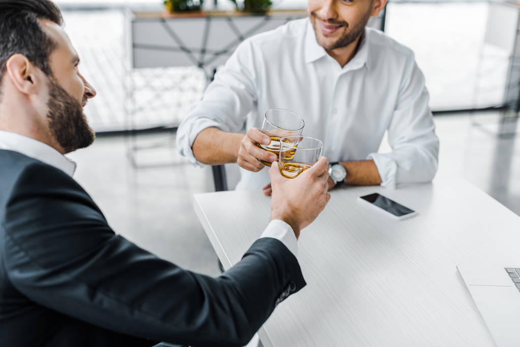 barbudo hombre de negocios tostando con whisky mientras está sentado en la oficina moderna con su compañero de trabajo
 - Foto, Imagen