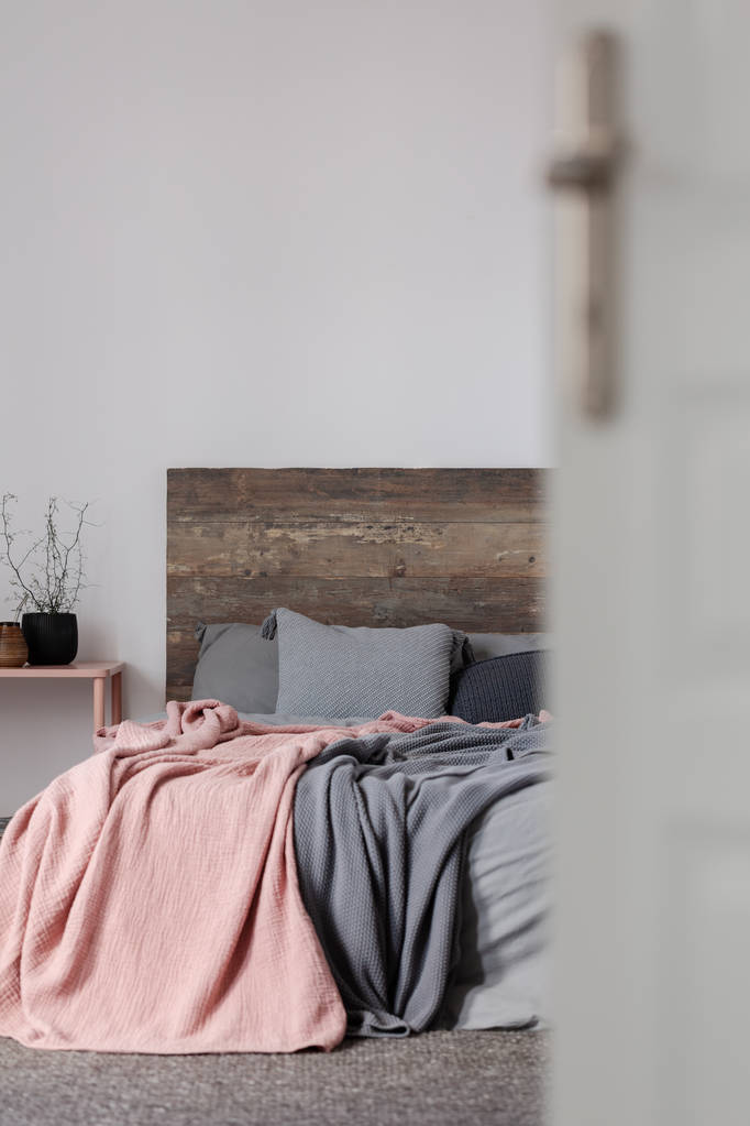 Pastel pink and grey blanket on grey bedding of king size bed with wooden headboard - Photo, Image