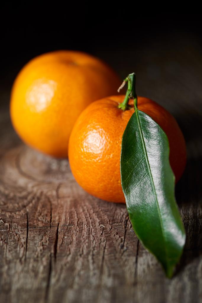 Selektywny fokus z zielonych liści na smaczny mandarynki na drewnianym stole  - Zdjęcie, obraz