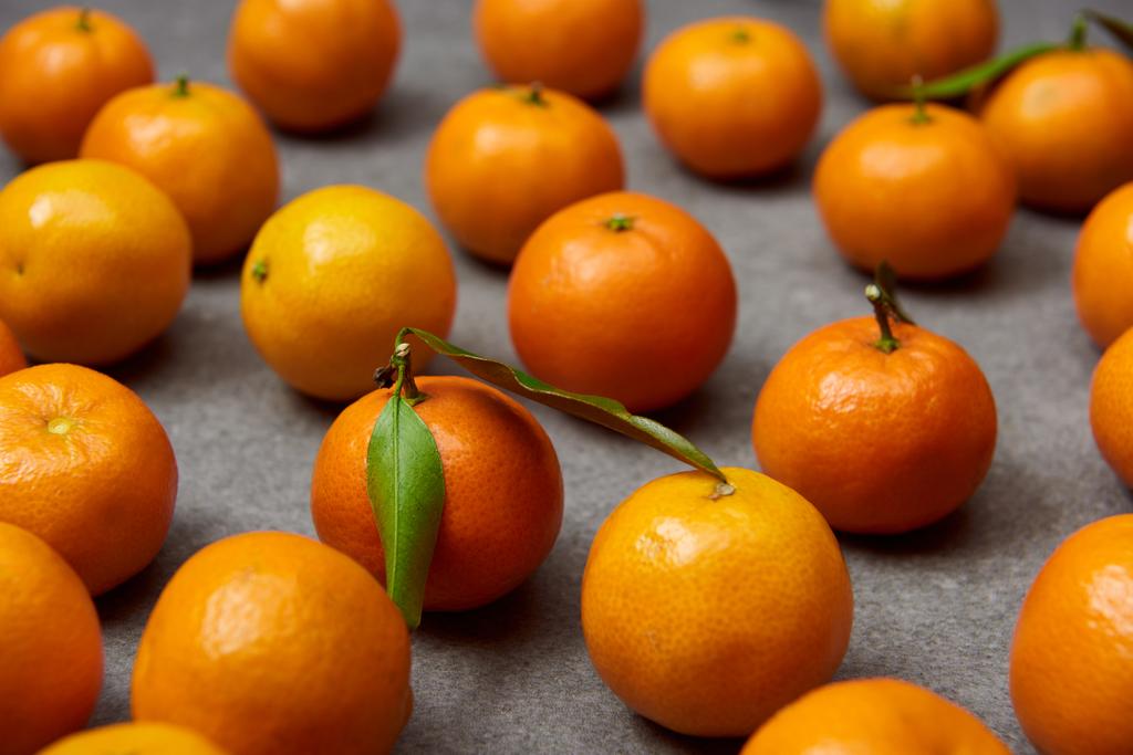 selective focus of organic orange tangerines with green leaves on grey table - Photo, Image
