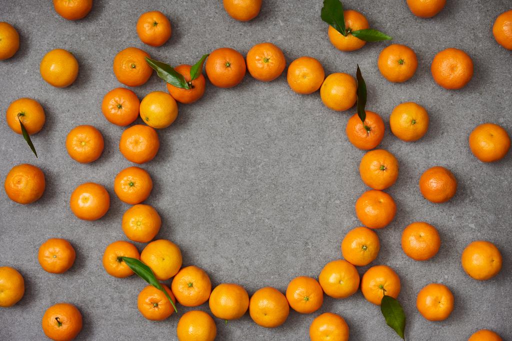 bovenaanzicht van zoete mandarijnen met groene bladeren op grijze tafel - Foto, afbeelding
