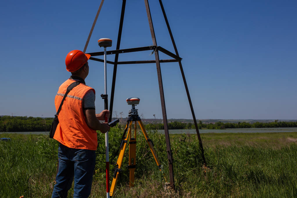 Профессиональный землемер измеряет наземный контрольный пункт с помощью GPS-ровера. Зеленое поле на заднем плане
 - Фото, изображение