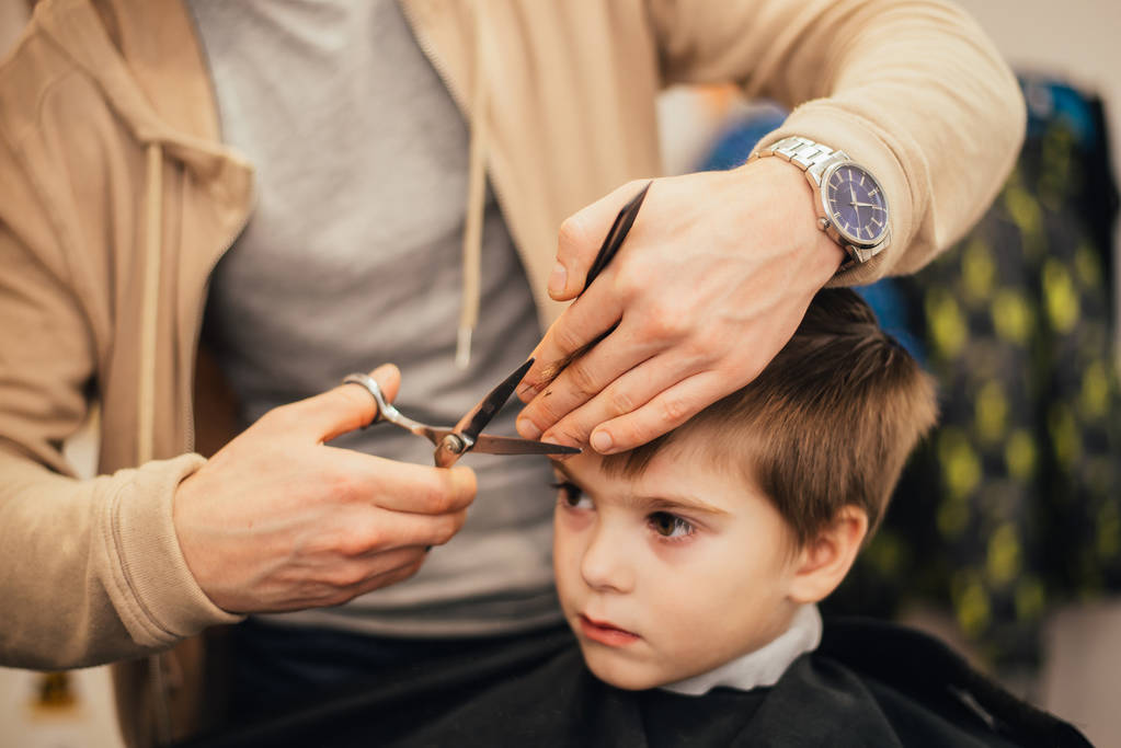 bijgesneden afbeelding van kapper maken van kapsel van kleine jongen op salon - Foto, afbeelding