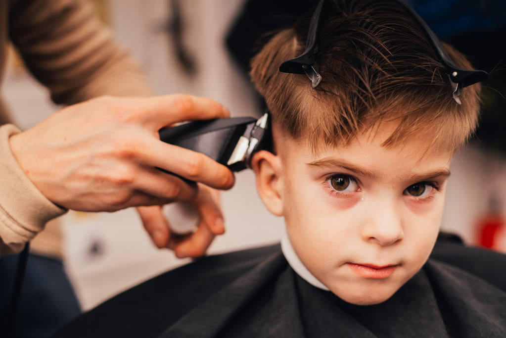 обрезанный образ парикмахера, делающего стрижку маленького мальчика в салоне
 - Фото, изображение