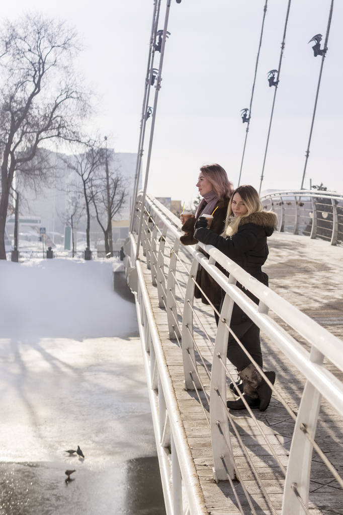 zwei Frauen mit Tassen Kaffee auf der Brücke im Winter - Foto, Bild