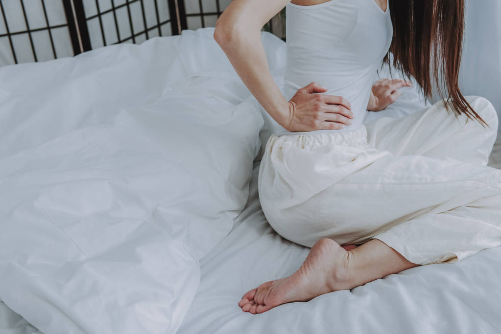 Giovane sensazione di dolore femminile sul letto leggero morbido
 - Foto, immagini