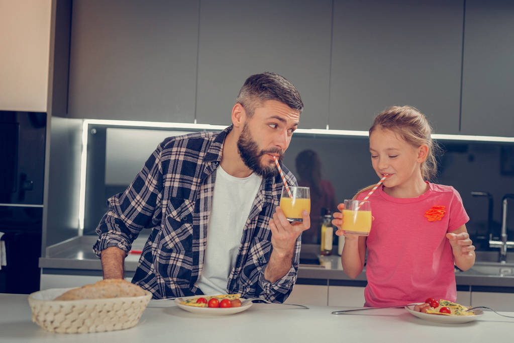 Barbudo hombre alto en una camisa a cuadros y su linda hija disfrutando del desayuno
 - Foto, Imagen