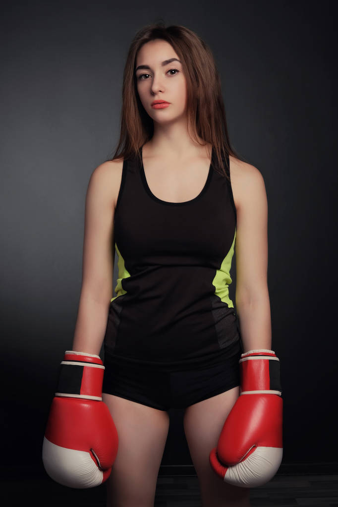 Chica de fitness joven con guantes de bloxing mirando a la cámara sobre el arte de fondo negro
 - Foto, Imagen