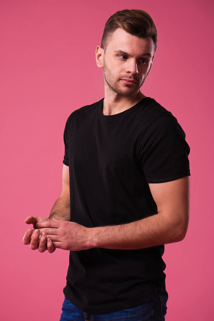 Όμορφο κομψό αυτοπεποίθηση και σοβαρό άνδρα σε μαύρο t-shirt θέτοντας σε ροζ φόντο - Φωτογραφία, εικόνα