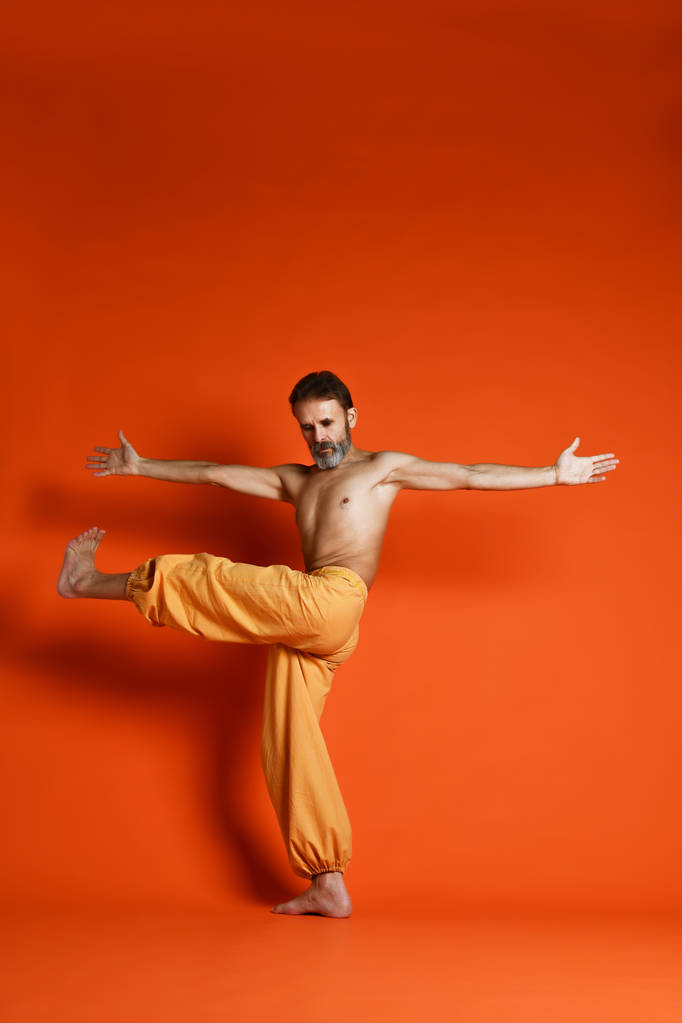 Stary człowiek Praktykuje jogę robi, stretching ćwiczenia na pomarańczowym tle - Zdjęcie, obraz