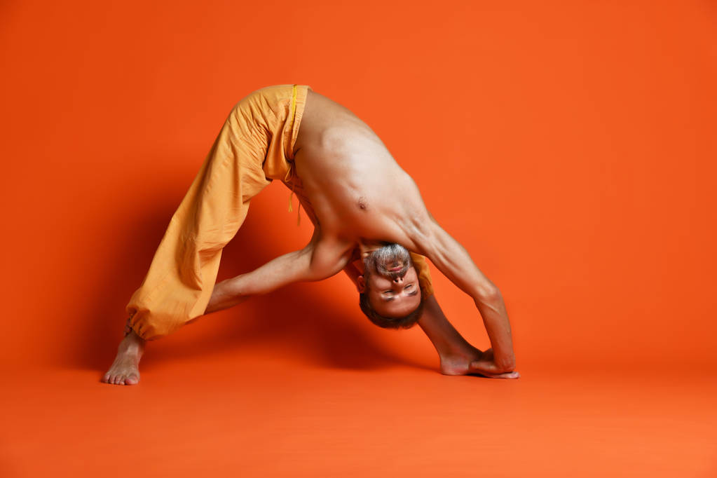 Stary człowiek Praktykuje jogę robi, stretching ćwiczenia na pomarańczowym tle - Zdjęcie, obraz
