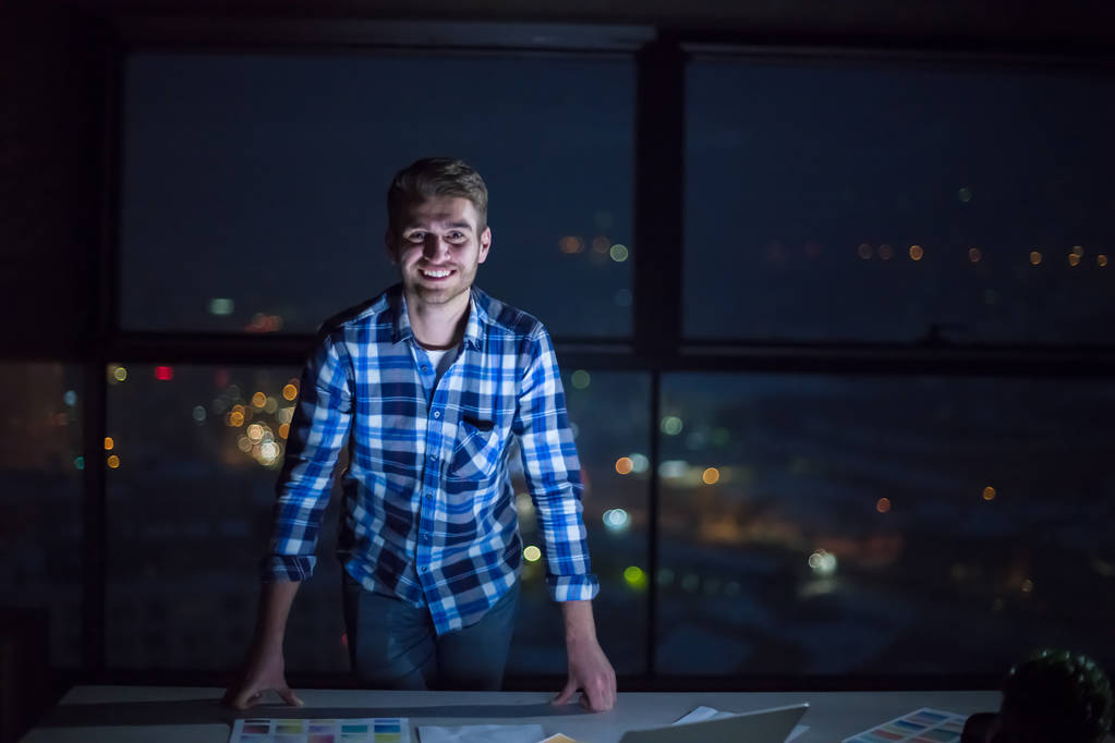 Porträt eines jungen männlichen Ingenieurs auf der Baustelle bei der Überprüfung von Dokumenten und Geschäftsabläufen am Laptop in einem neuen Startup-Büro in der Nacht - Foto, Bild