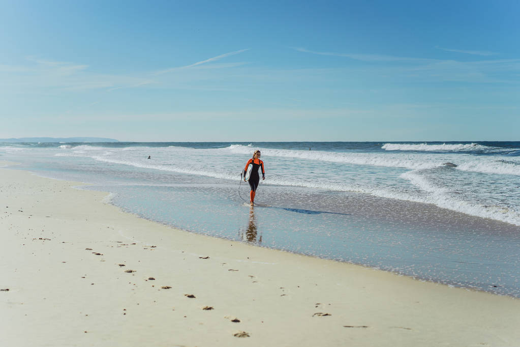 κορίτσι σερφ στις ακτές της ωκεανό σε ένα υγρό κοστούμι με surf σκάφους, Nazar, Πορτογαλία. - Φωτογραφία, εικόνα