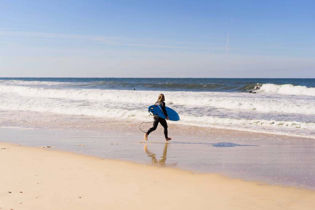 человек с доской для серфинга на берегу океана. Сёрфер в мокром костюме. Назаре, Португалия
. - Фото, изображение