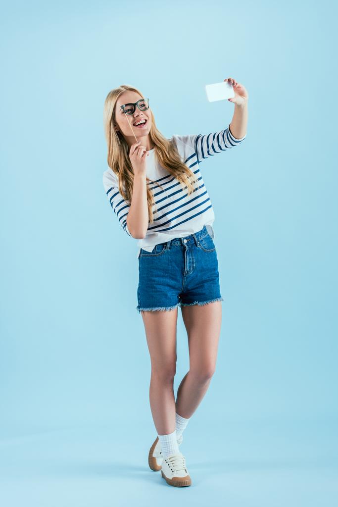 Προβολή πλήρους μήκους γέλιο γυναίκα λήψης selfie με γυαλιά παιχνίδι σε μπλε φόντο - Φωτογραφία, εικόνα