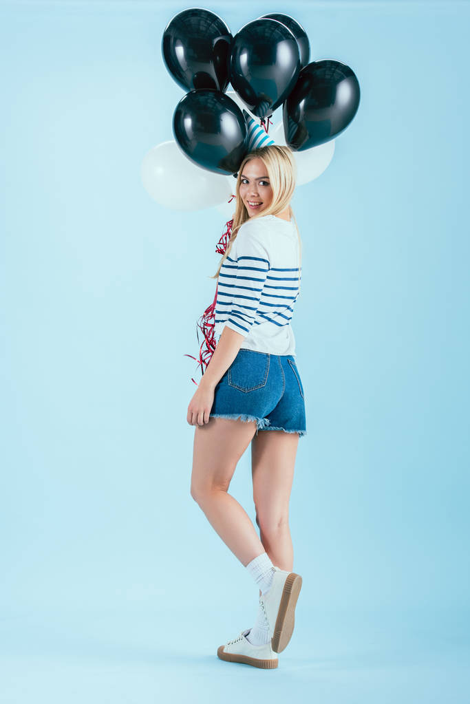 Opgewekt meisje met bos van partij ballonnen kijken over de schouder op blauwe achtergrond - Foto, afbeelding