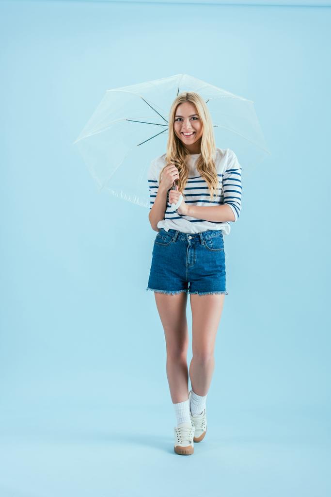 fröhliches blondes Mädchen mit Regenschirm auf blauem Hintergrund - Foto, Bild