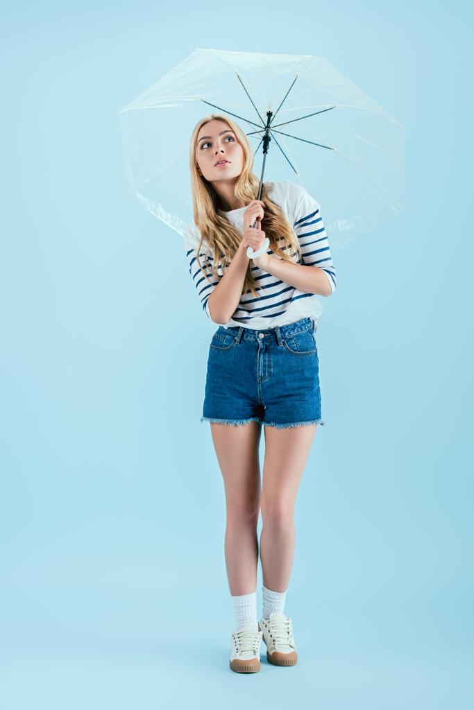 青の背景に傘を保持しているカジュアルな服装の女性 - 写真・画像