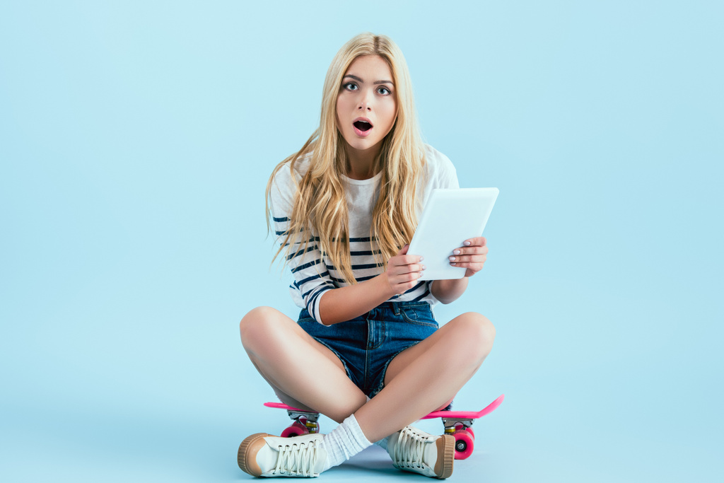 Döbbenve lány ül a kék háttér longboard digitális tabletta - Fotó, kép