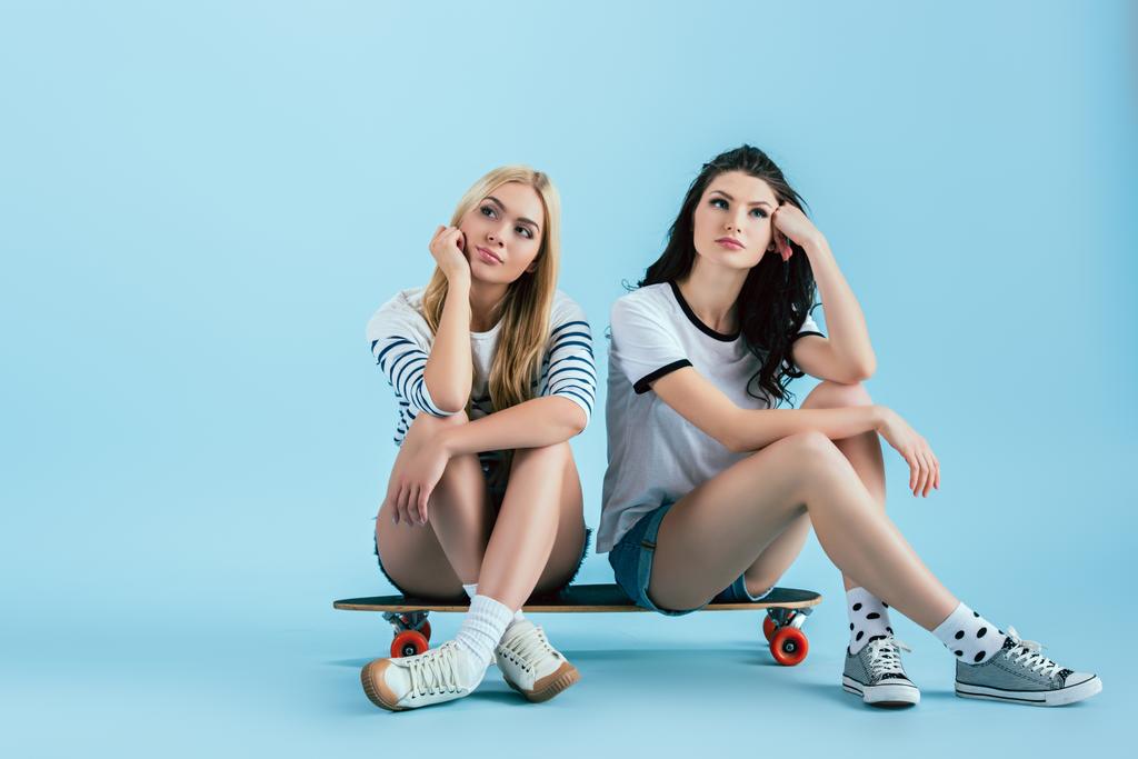 nachdenkliche Mädchen auf Longboard sitzend und proppenvolle Gesichter mit Händen auf blauem Hintergrund - Foto, Bild