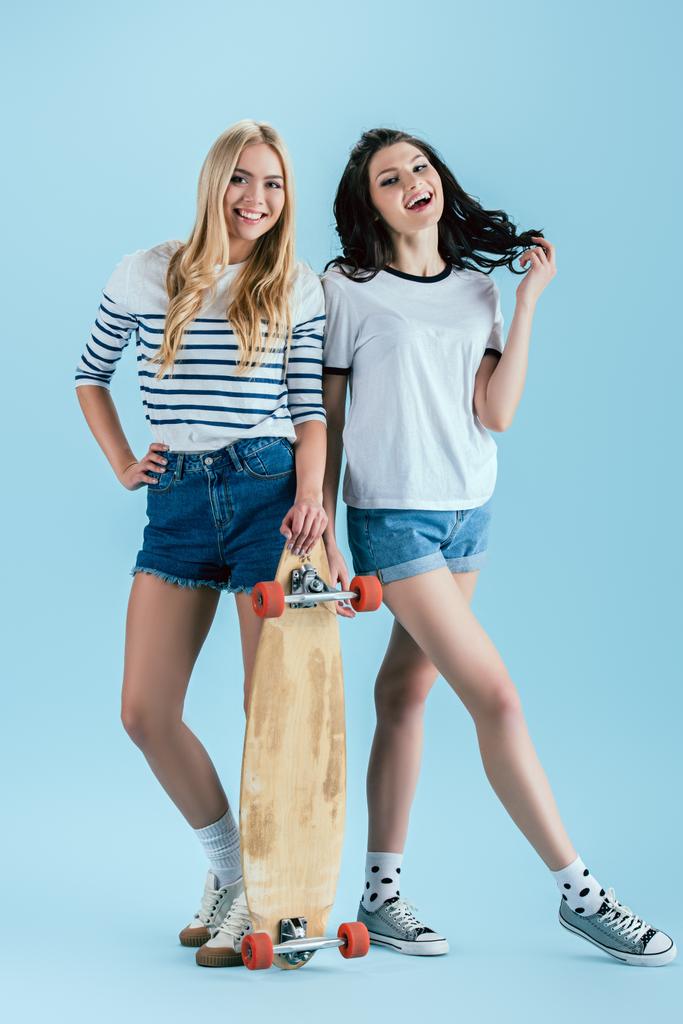 Impresionantes chicas posando con longboard de madera sobre fondo azul
 - Foto, Imagen